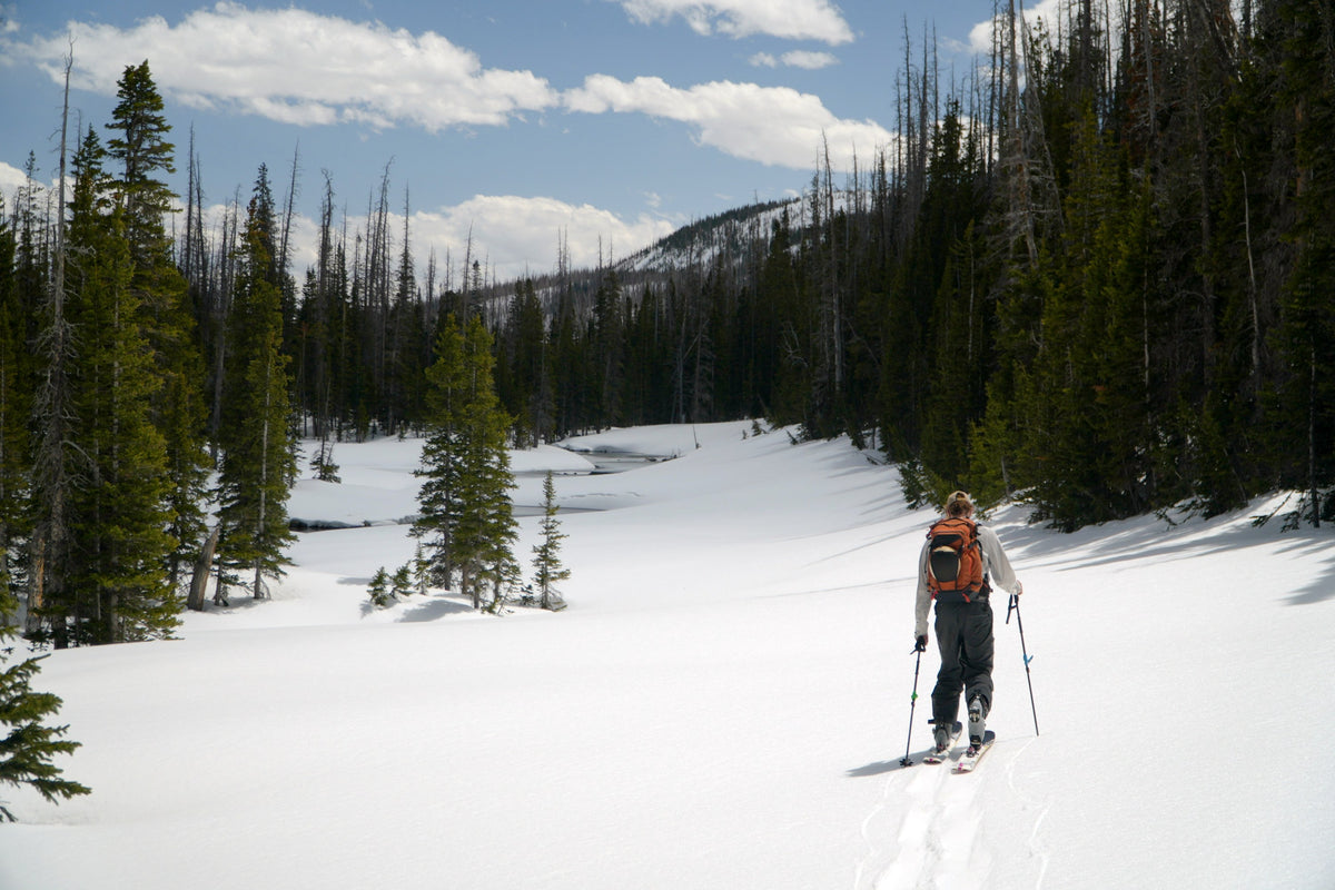 Backcountry skier skinning across a snowy meadow in technical outerwear